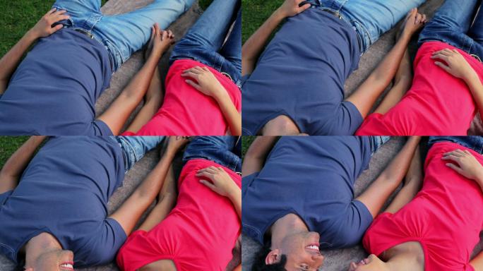 一对幸福的情侣躺在毯子上，手牵着手在公园里