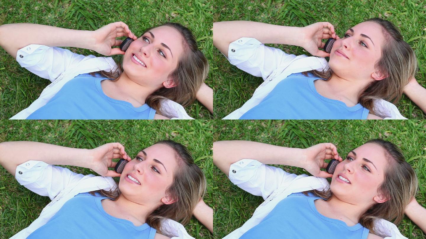 一个面带微笑的女人躺在草地上打电话