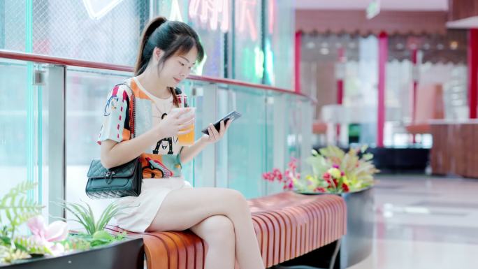 4K年轻女性在商场长椅坐着看手机喝冷饮