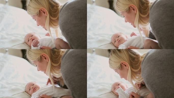 一位妇女抱着并揉着一个精力充沛的婴儿，当他躺在白色的床上时，婴儿正在移动他的胳膊和腿