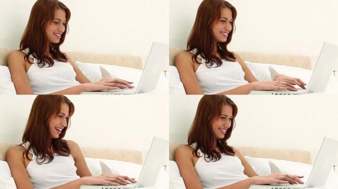 一个女性坐在床上玩笔记本电脑