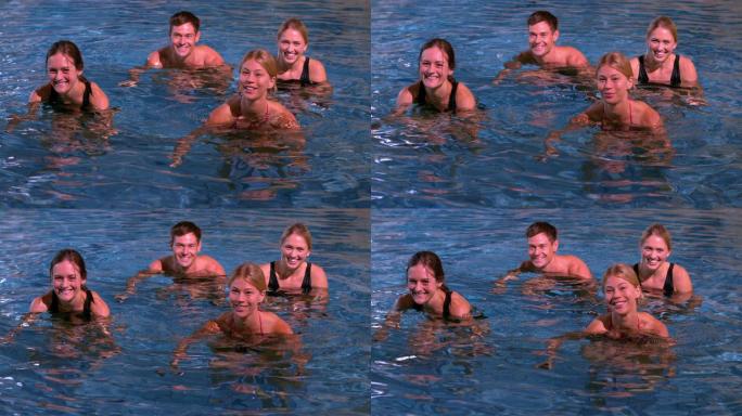 健身班在游泳池里做水中有氧运动，对着慢镜头微笑