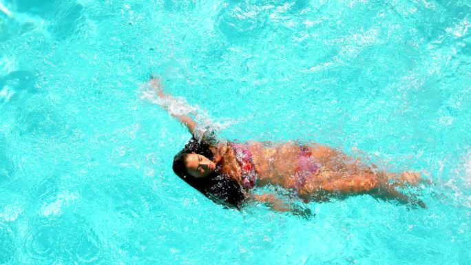 在一个阳光明媚的日子里，黑发女子慢动作地游过游泳池