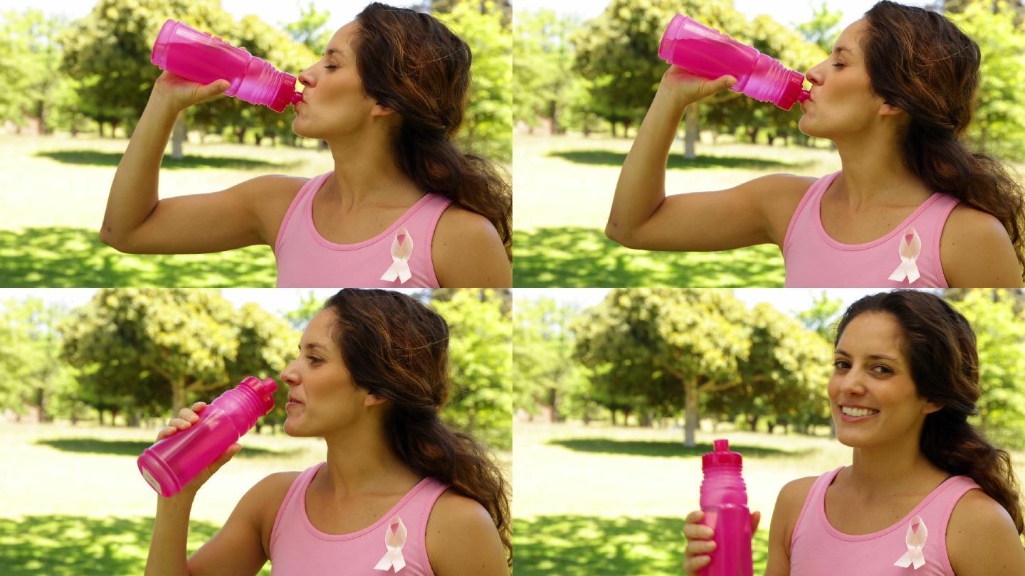 一个快乐的女人穿着粉红色的衣服来宣传乳腺癌，在阳光明媚的日子里喝着水
