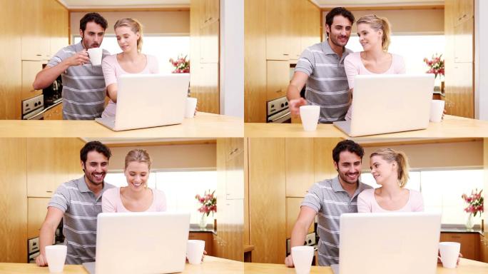 微笑的情侣站在厨房看笔记本电脑