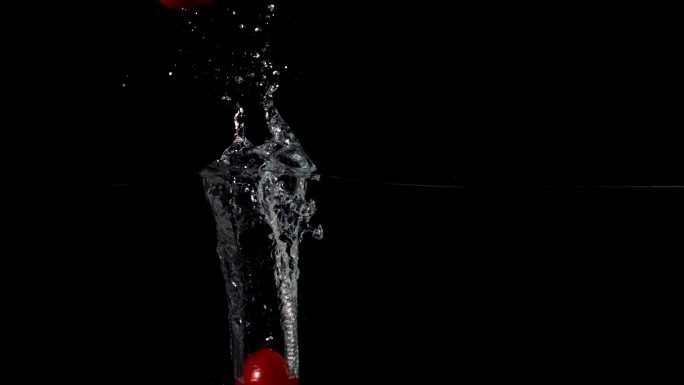 在黑色背景的慢镜头中，樱桃番茄落在水中