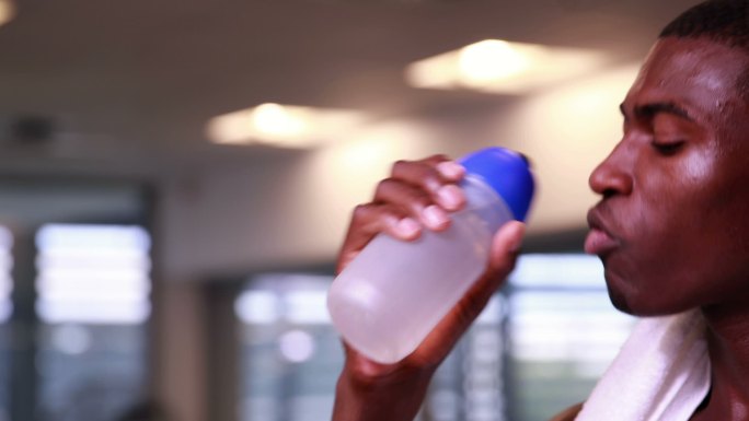 健身房里，喝着水对着镜头微笑的健康男子