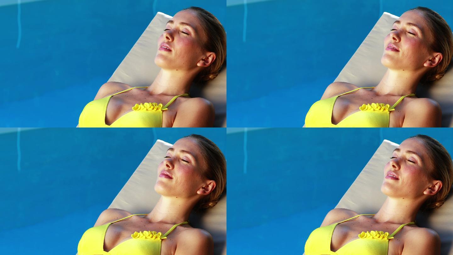 在阳光明媚的日子里，美丽的金发女郎在比基尼享受阳光泳池边
