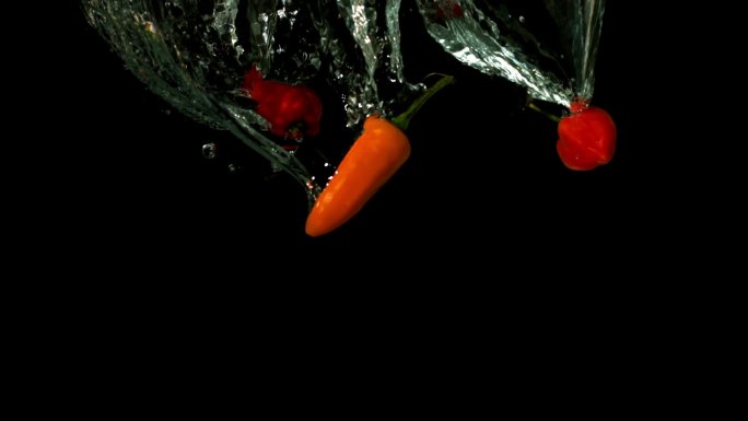 在黑色背景的慢镜头中，辣椒落在水中