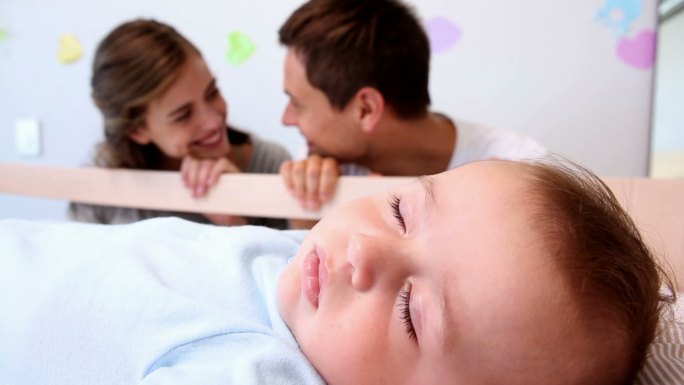 快乐的父母在卧室里照看着婴儿床里的儿子