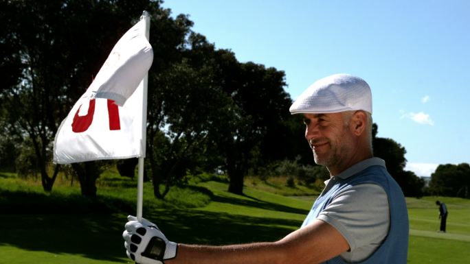 微笑的高尔夫球手举着第十八洞旗在高尔夫球场的慢动作