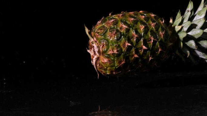 慢镜头中，菠萝旋转并落在潮湿的黑色表面上