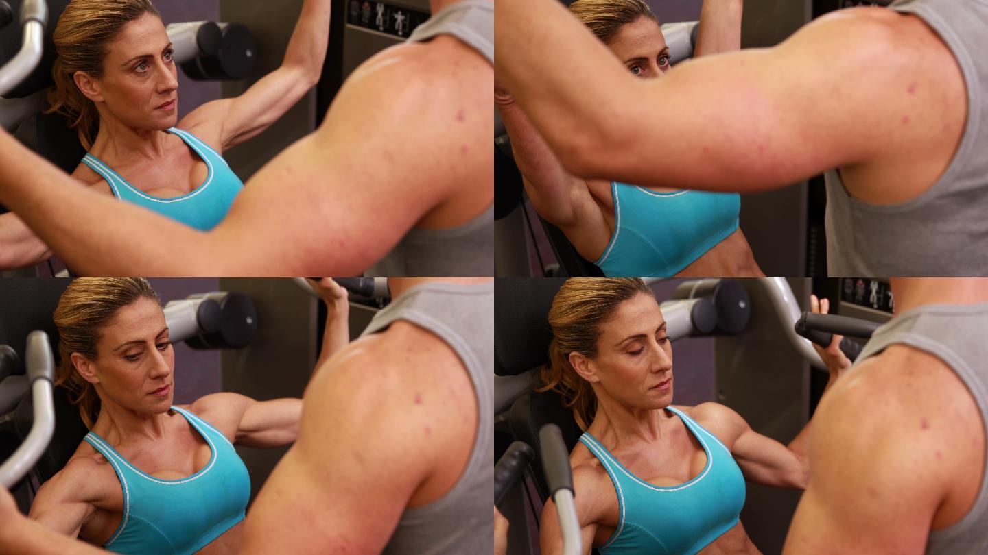 在健身房里和她的教练一起使用举重机锻炼手臂