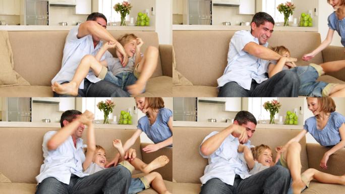 父亲和女儿在客厅的沙发上给小男孩搔痒