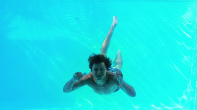 快乐的男人在他的假期在游泳池里跳向镜头挥手