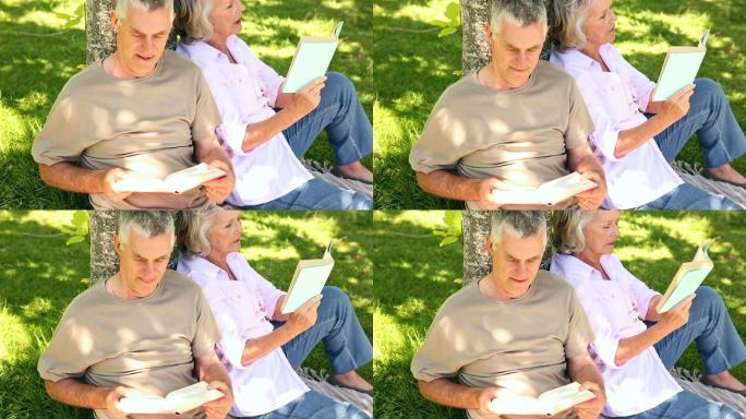 一对退休夫妇倚着树在花园里看书