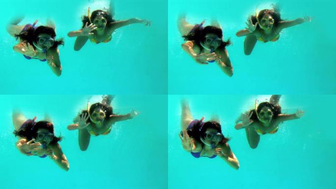 在慢镜头中，快乐的朋友们在水下戴着通气管挥手