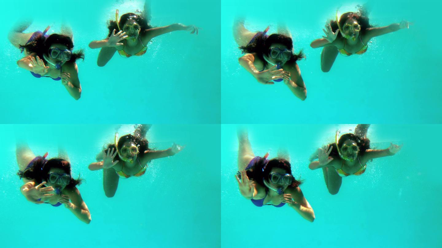 在慢镜头中，快乐的朋友们在水下戴着通气管挥手