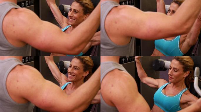 在健身房里和她的教练一起使用举重机锻炼手臂