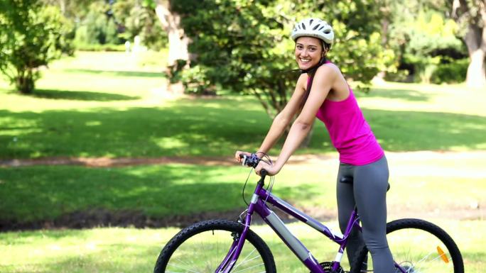 一个健康的女孩在一个阳光明媚的日子里在公园里骑自行车
