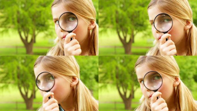 Cute little girl using magnifying glass in park on