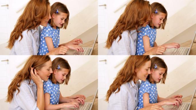 小女孩和她漂亮的妈妈在客厅的桌子上使用笔记本电脑
