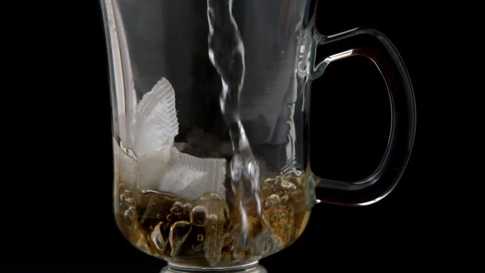 慢动作将热水倒在玻璃杯中的茶包上
