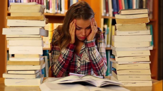 压力大的学生在图书馆里学习和做笔记，周围都是书