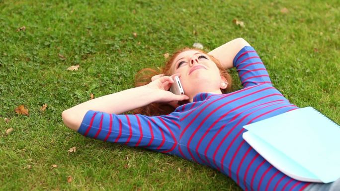 微笑的学生躺在草地上打电话在大学校园