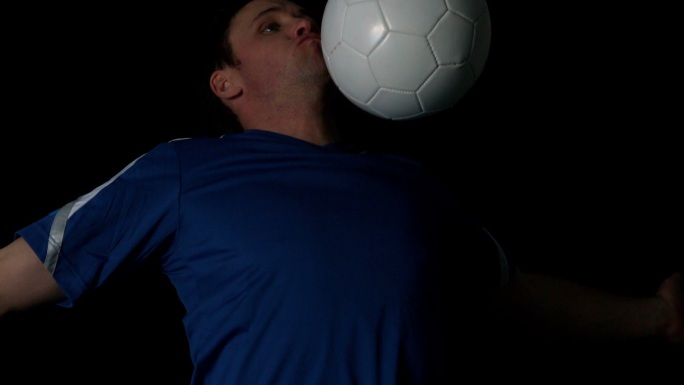 足球运动员控制球与他的胸部在黑色背景的慢动作