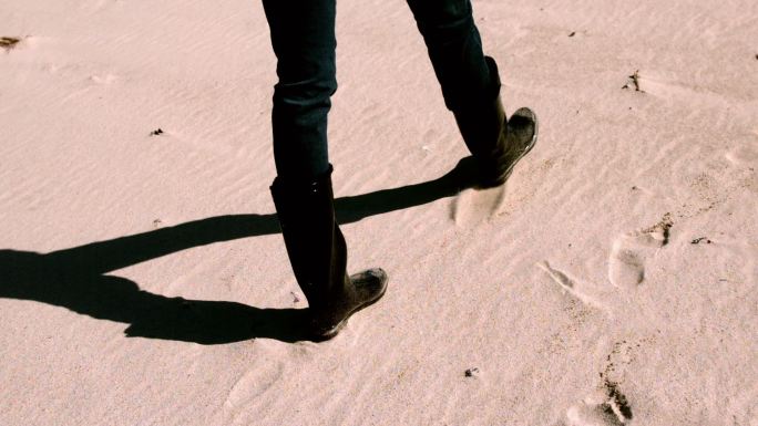 穿着靴子在沙滩上慢镜头行走的女人