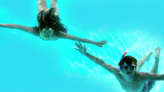 在慢镜头中，一对快乐的夫妇穿着通气管在游泳池水下