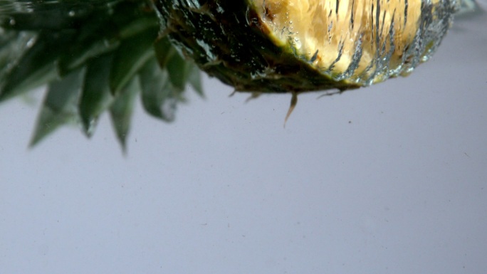 在慢动作的白色背景下，菠萝一半落在水中