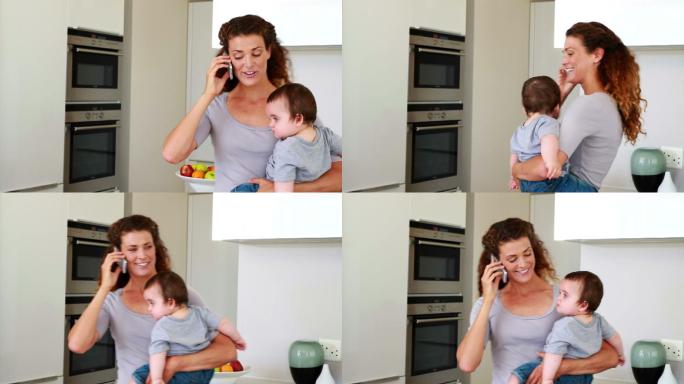 妈妈抱着她快乐的小男孩，在厨房里打电话