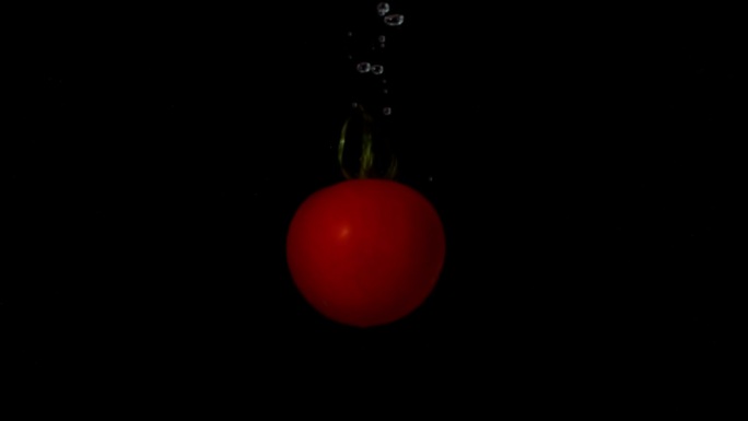 在慢动作的黑色背景下，番茄落在水中