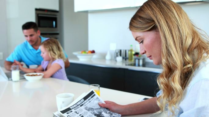 当家人在厨房里吃早餐时，妈妈在看报纸