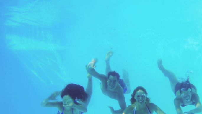 四个朋友在度假时跳进游泳池挥手