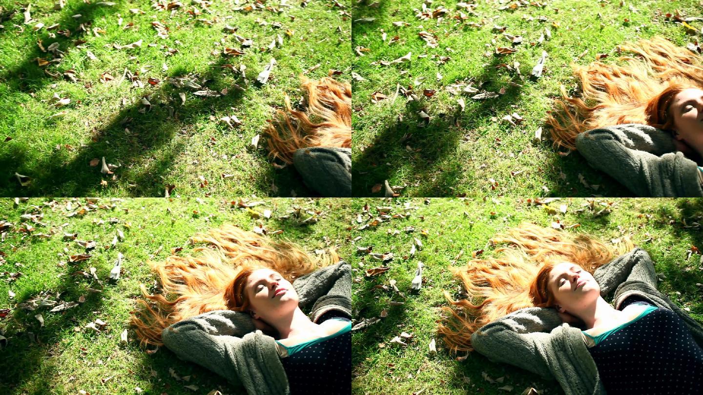 漂亮的红发姑娘在灿烂的阳光下在草坪上打盹
