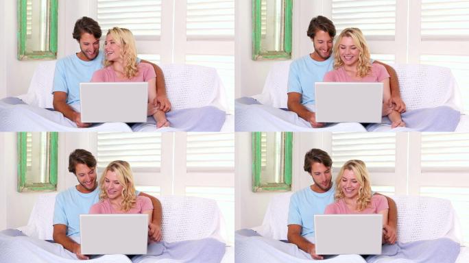 一对夫妇坐在沙发上，盖着毯子，在客厅里用笔记本电脑