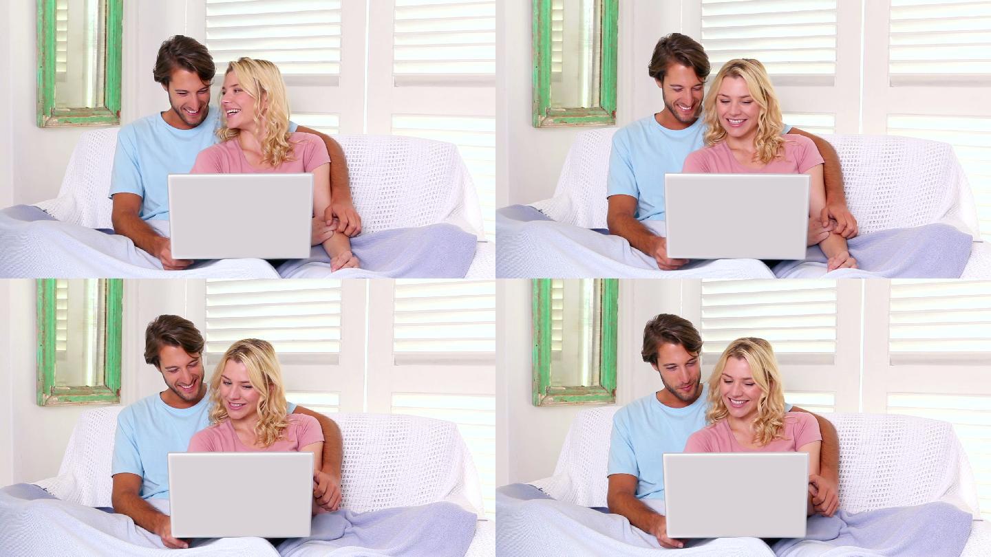一对夫妇坐在沙发上，盖着毯子，在客厅里用笔记本电脑