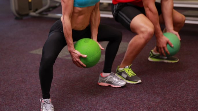 两个健康的人蹲在健身房与实心球