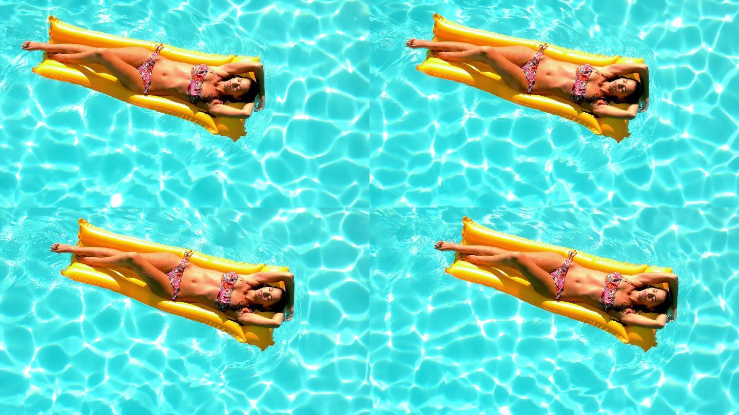 在一个阳光明媚的日子里，褐发女郎在气垫上漂过游泳池