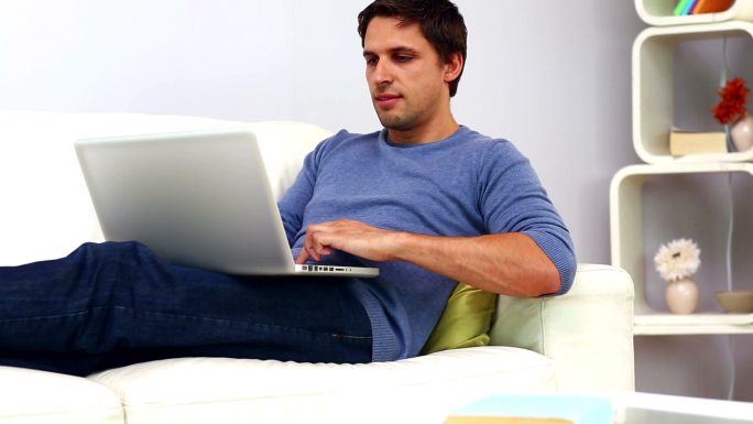 一个平静随意的人坐在明亮的客厅的沙发上用他的笔记本