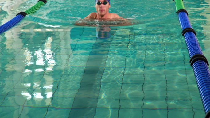 健身男子在休闲中心的游泳池里对着镜头做蛙泳和微笑