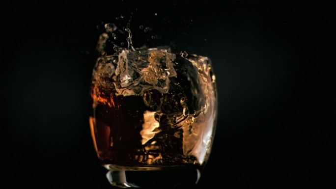 在黑色背景的威士忌中，冰块以超慢的动作下落