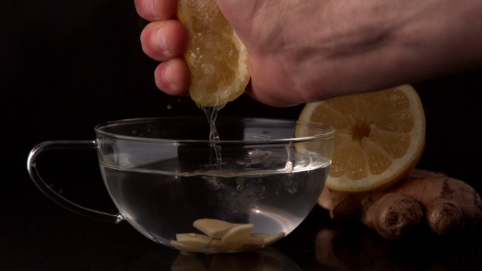 用手把柠檬慢动作挤进一杯热水和姜