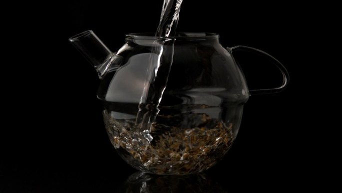 慢动作将水倒入玻璃茶壶，浇在松散的凉茶上