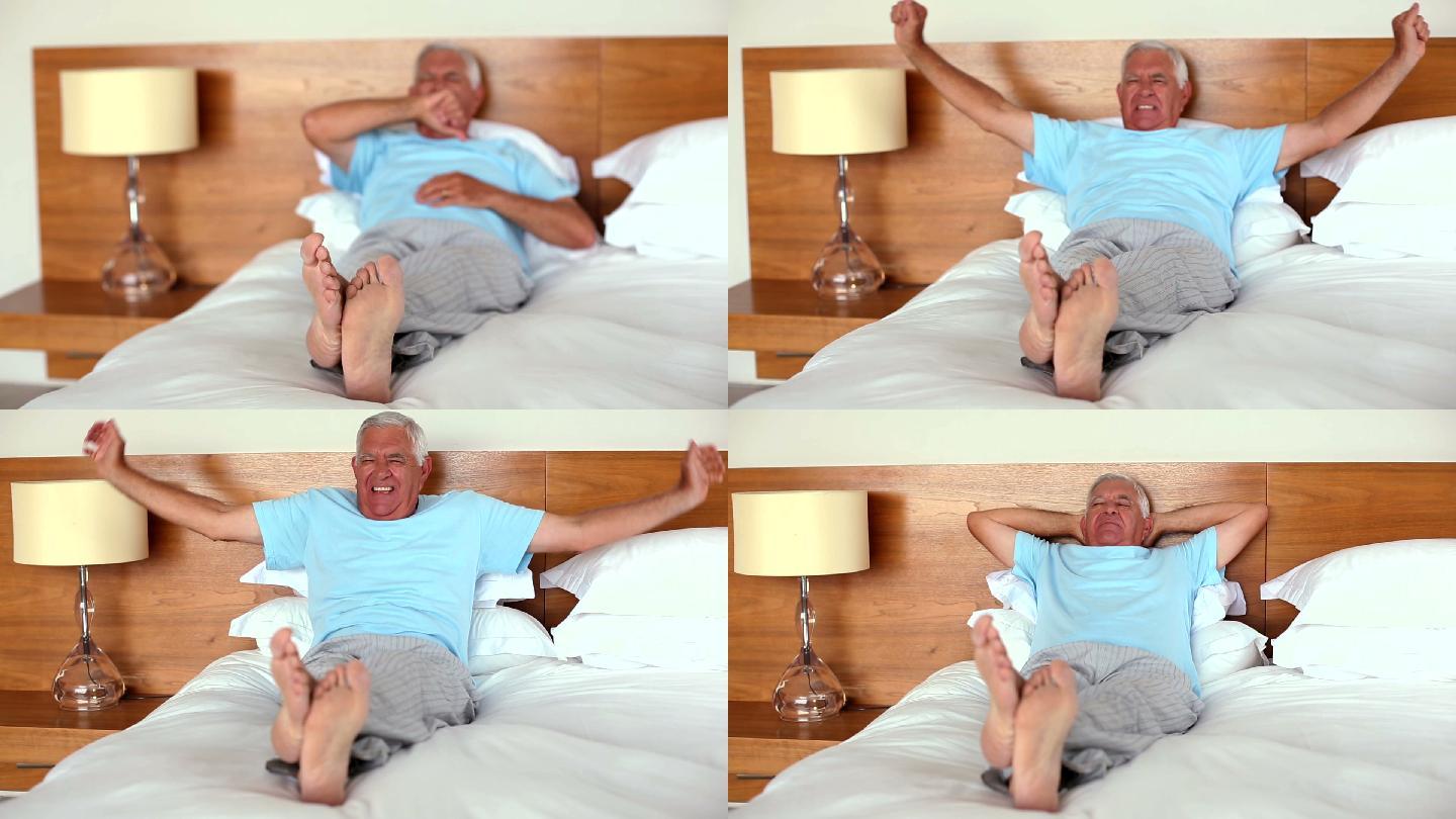 老人躺在床上打哈欠和伸懒腰在家里的卧室里