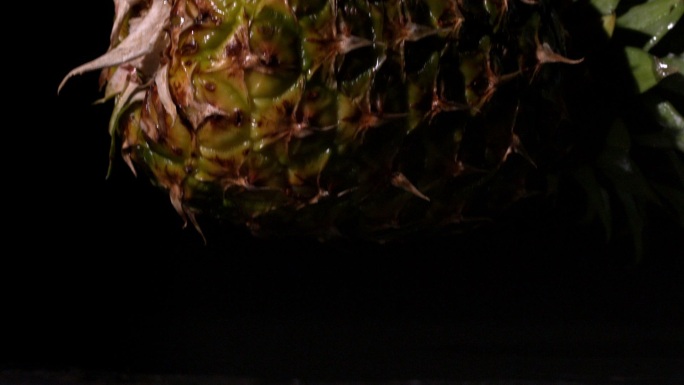 在慢镜头中，菠萝在黑色背景上落下并裂开
