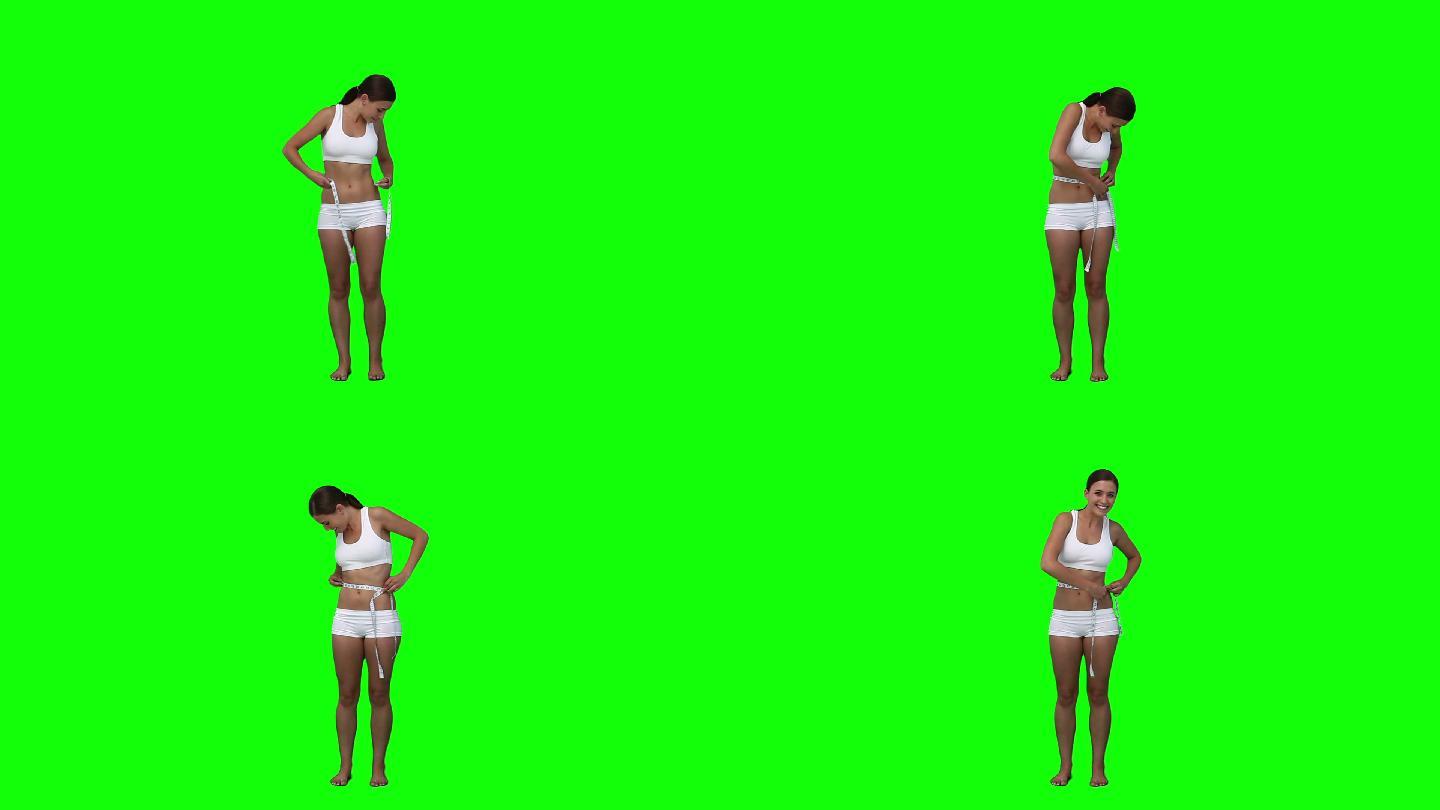 一个亚洲女性测量腰围，在绿色的背景下